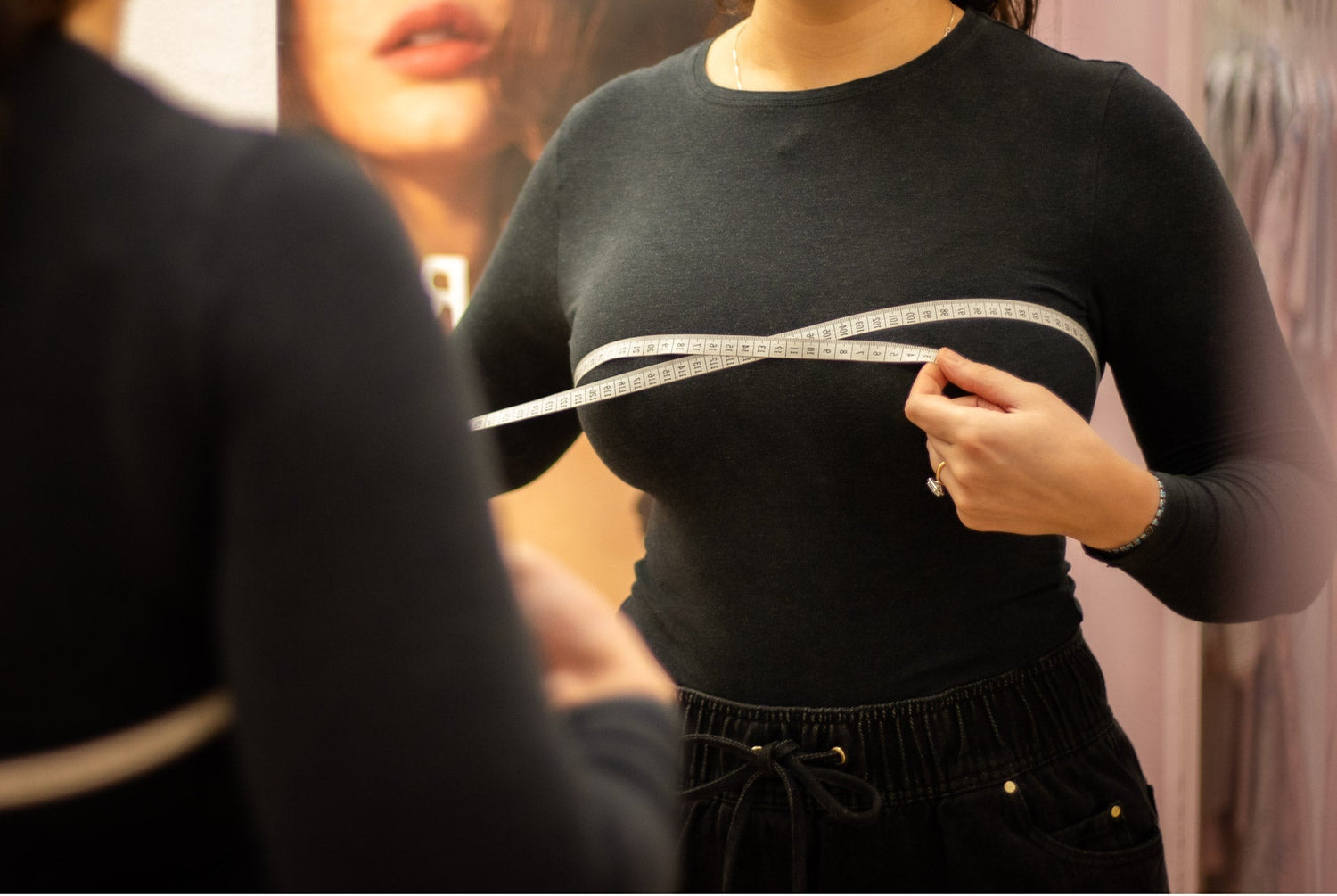 A white measuring tape with black numbers held across a woman’s chest for accurate bra size measurement.