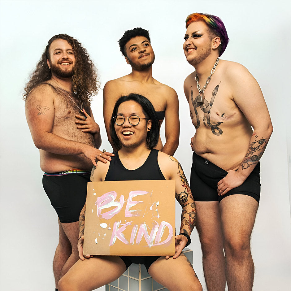 A handmade cardboard sign with be kind painted in pink and white marker with visible brush strokes from paxies