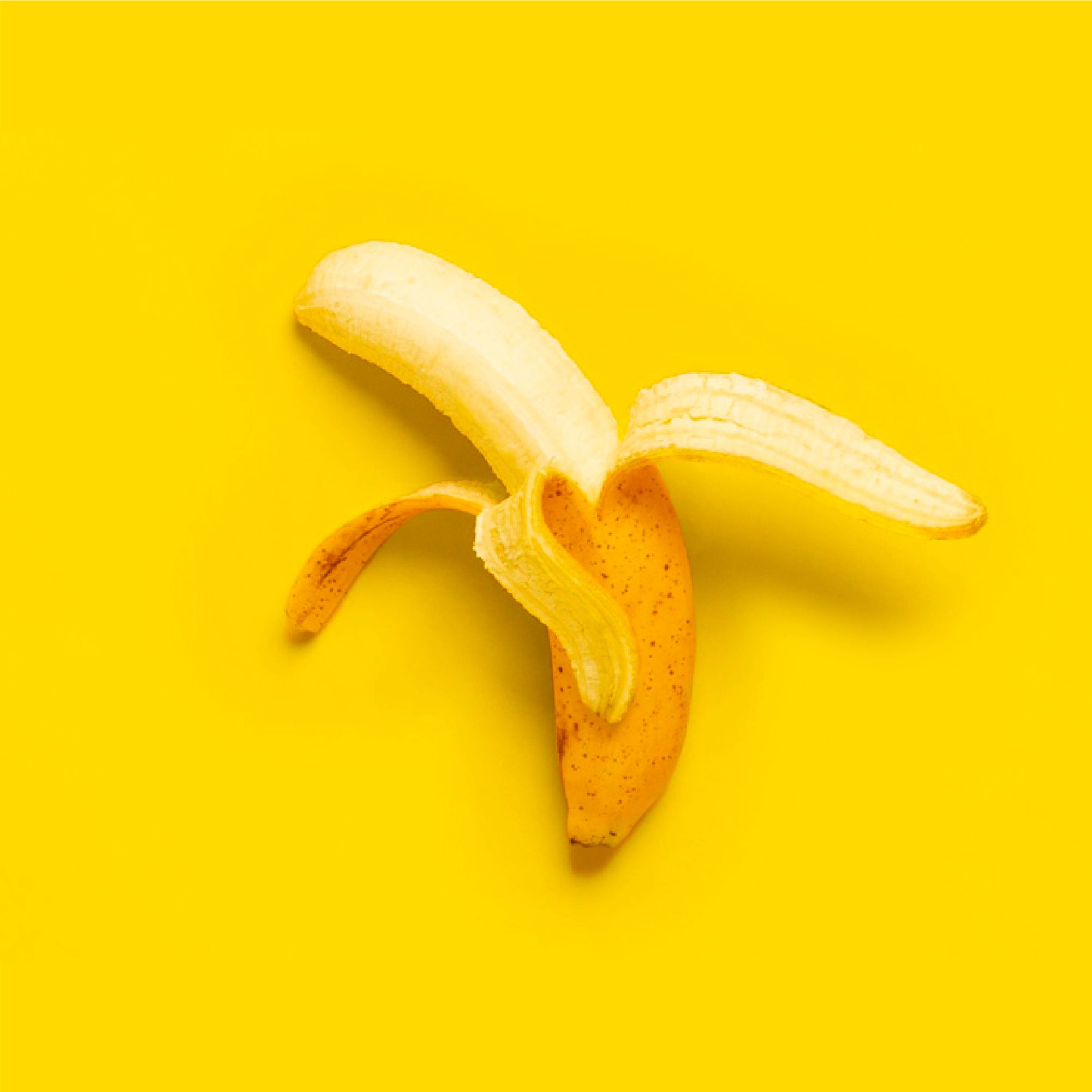 A partially peeled banana with a yellow peel and pale flesh against a vibrant yellow background.
