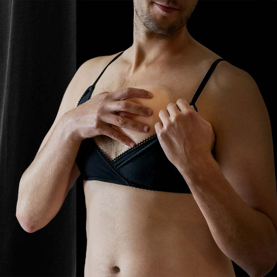 A man placing a breast form into his black lace bra on a dark background