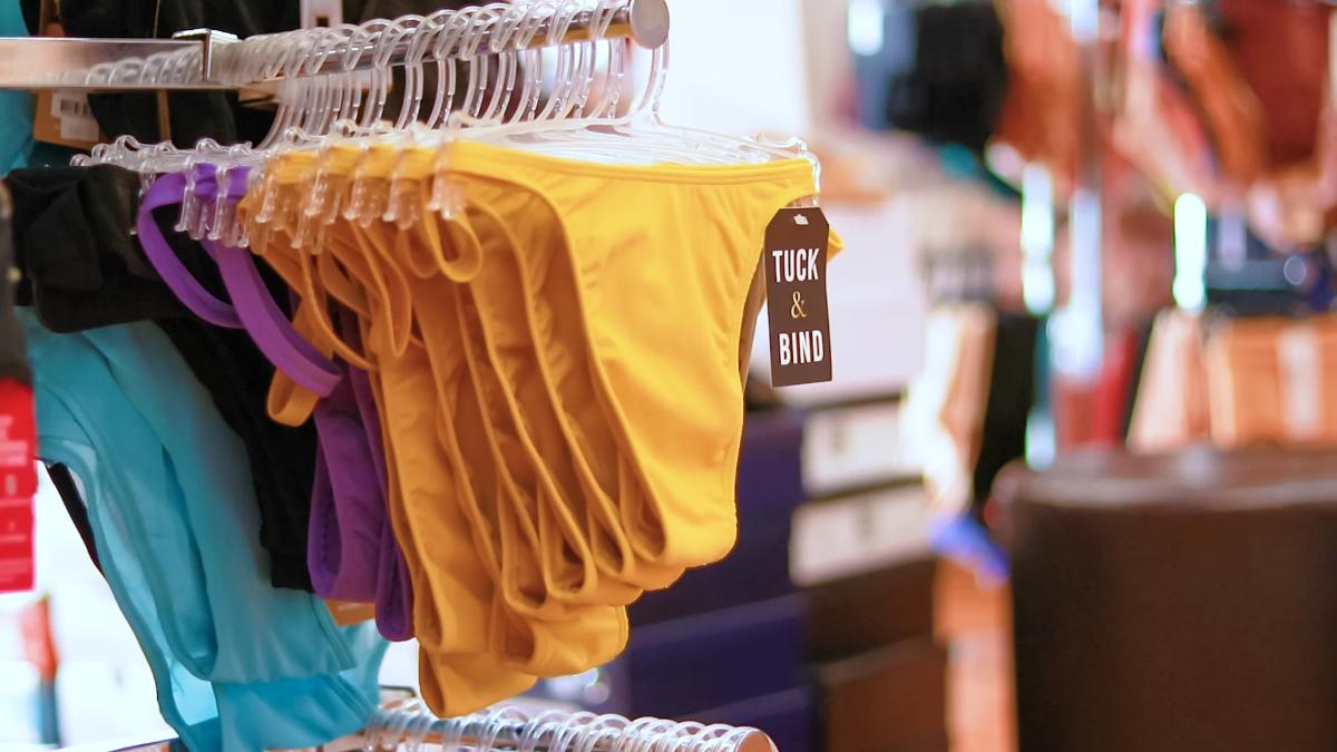 Yellow underwear on a rack with 'Tuck & Bind' label, surrounded by other colorful underwear.