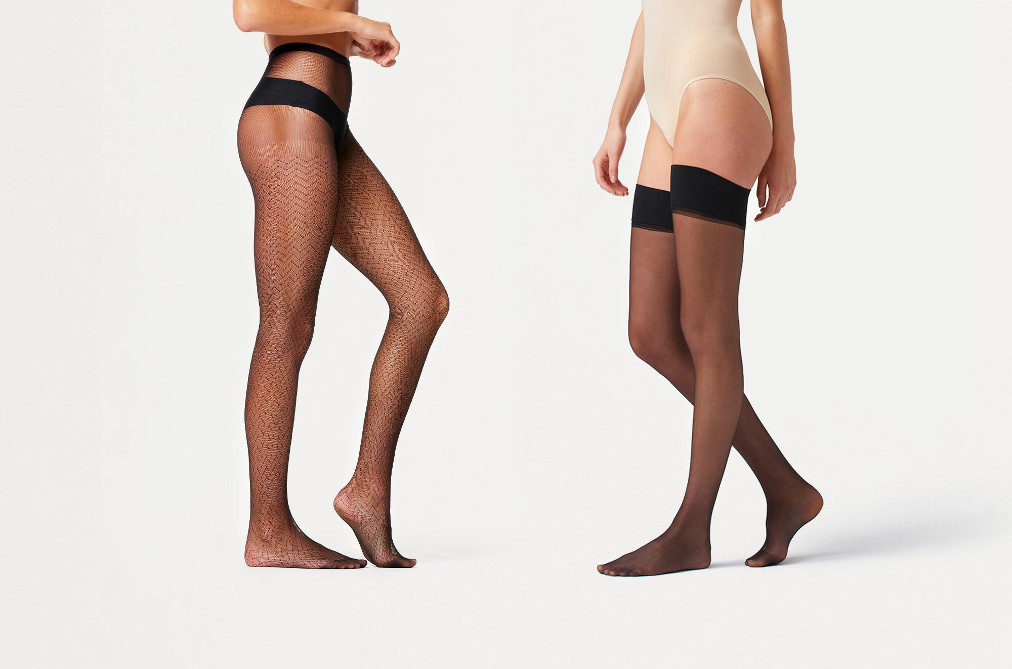 Two sets of legs wearing black hosiery on a white background