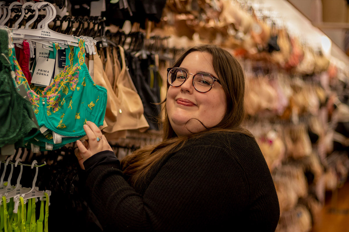 Bra fitter smiling at the camera while going through a wall of bras