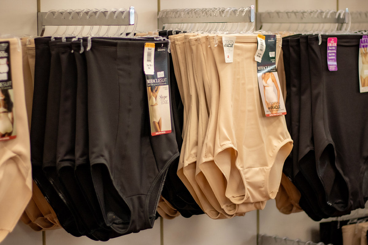 Black and beige plus size shapewear pants hanging on a rack with tags.