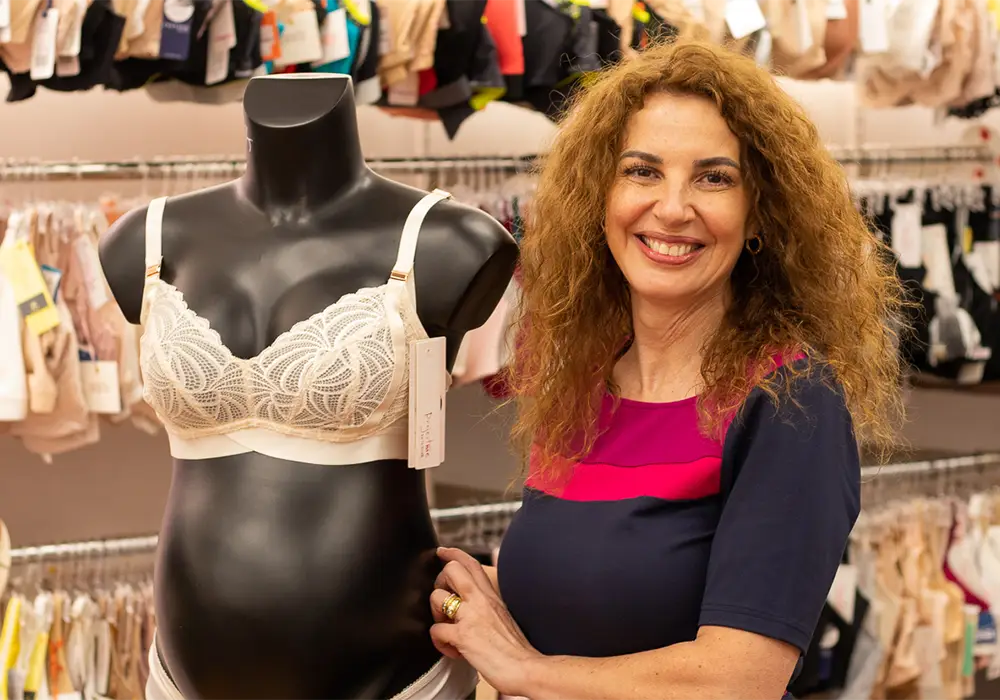 Maternity bra fitter standing next to a pregnant mannequin in a maternity bra.