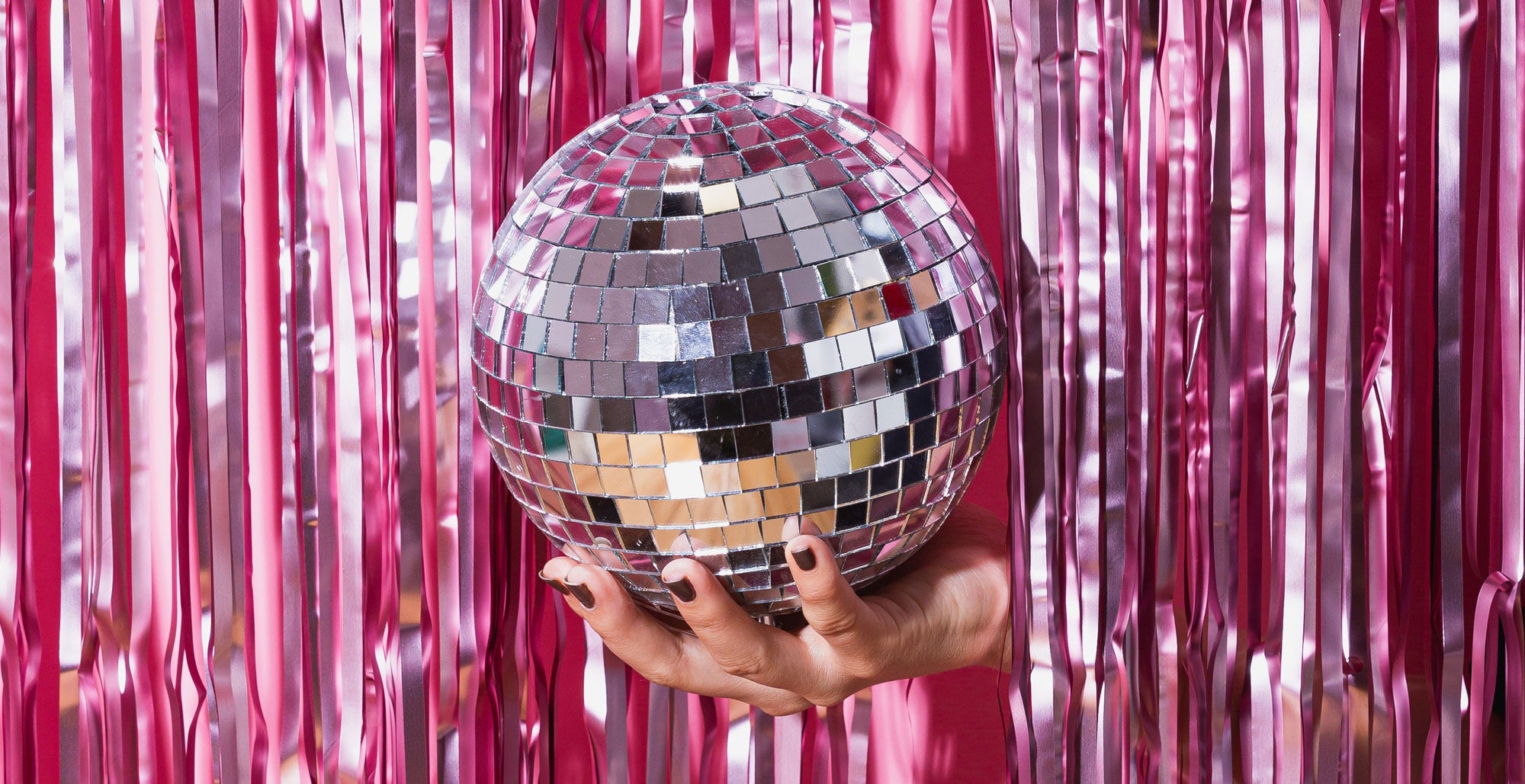 Hand holding disco ball infront of pink backdrop