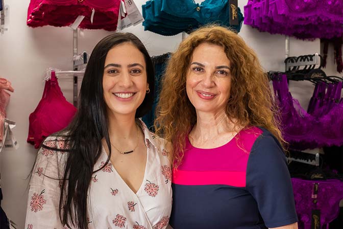 Two bra fitters smiling in front of a wall of colourful bras