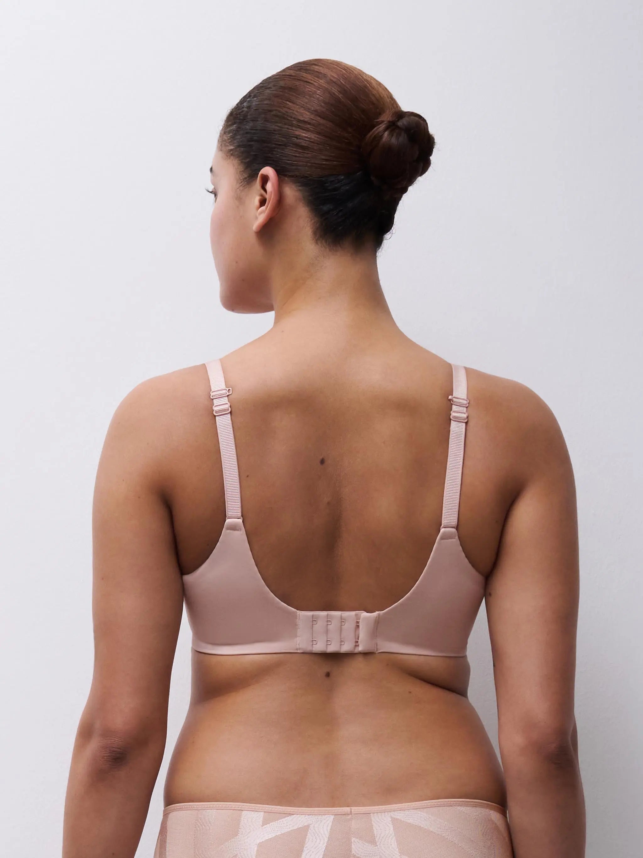 A soft blush pink glaze very covering underwire bra with adjustable straps and center back closure shown from the back
