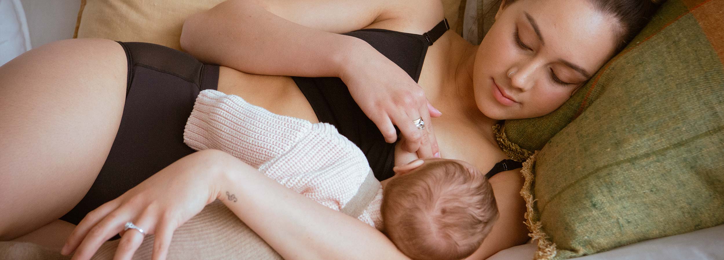 Woman in maternity lingerie breastfeeding baby on couch