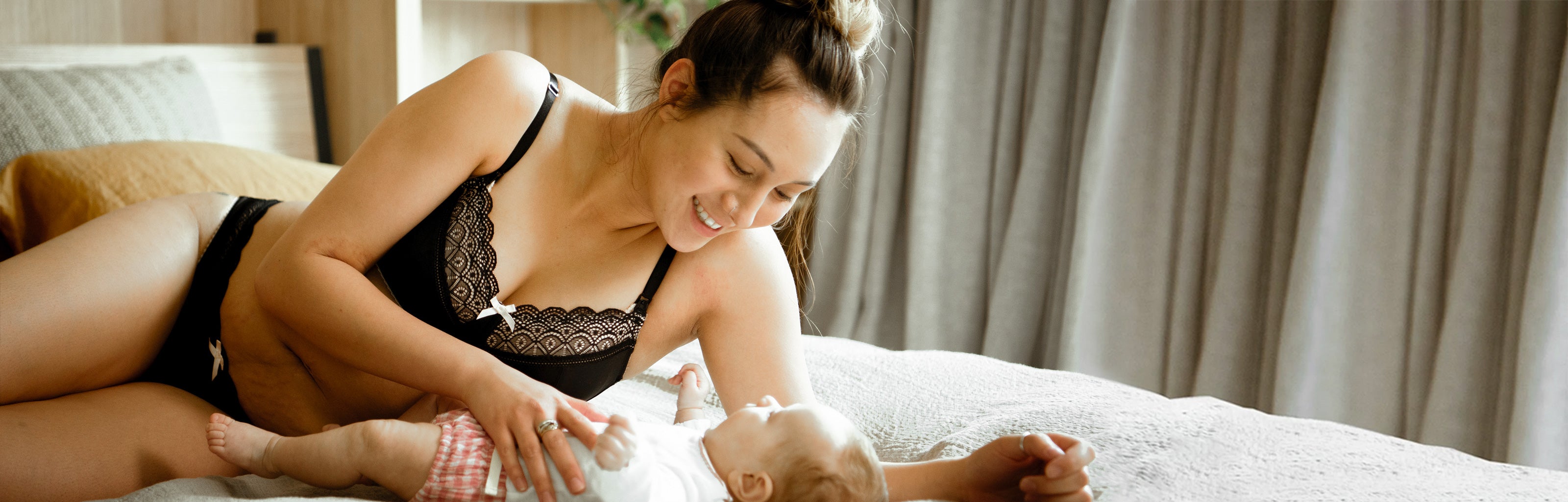 Woman in black maternity lingerie sitting on a bed with a baby