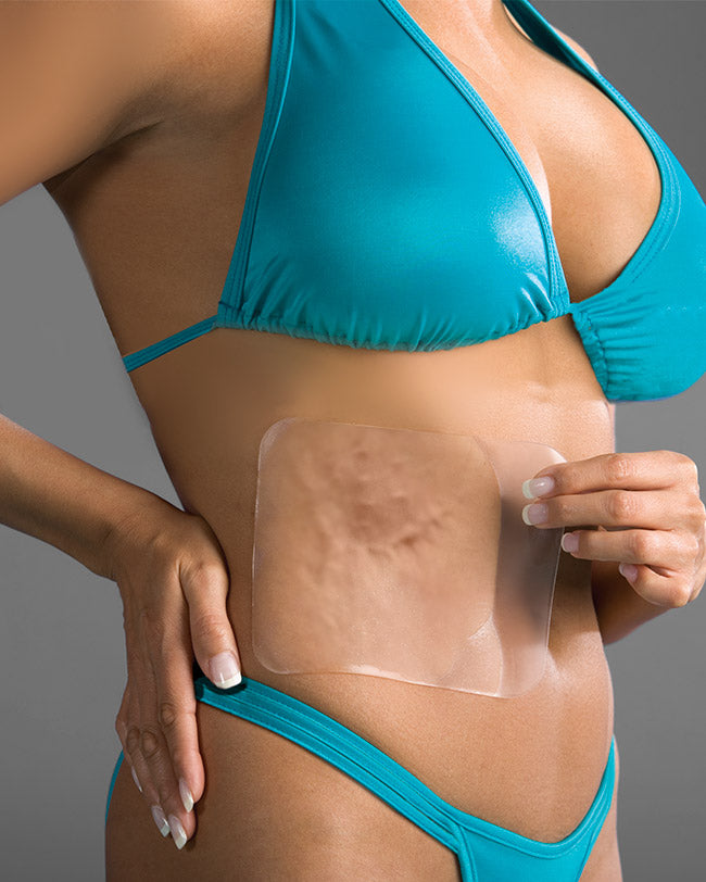 Woman in bathers applying silicone sheet to abdomen