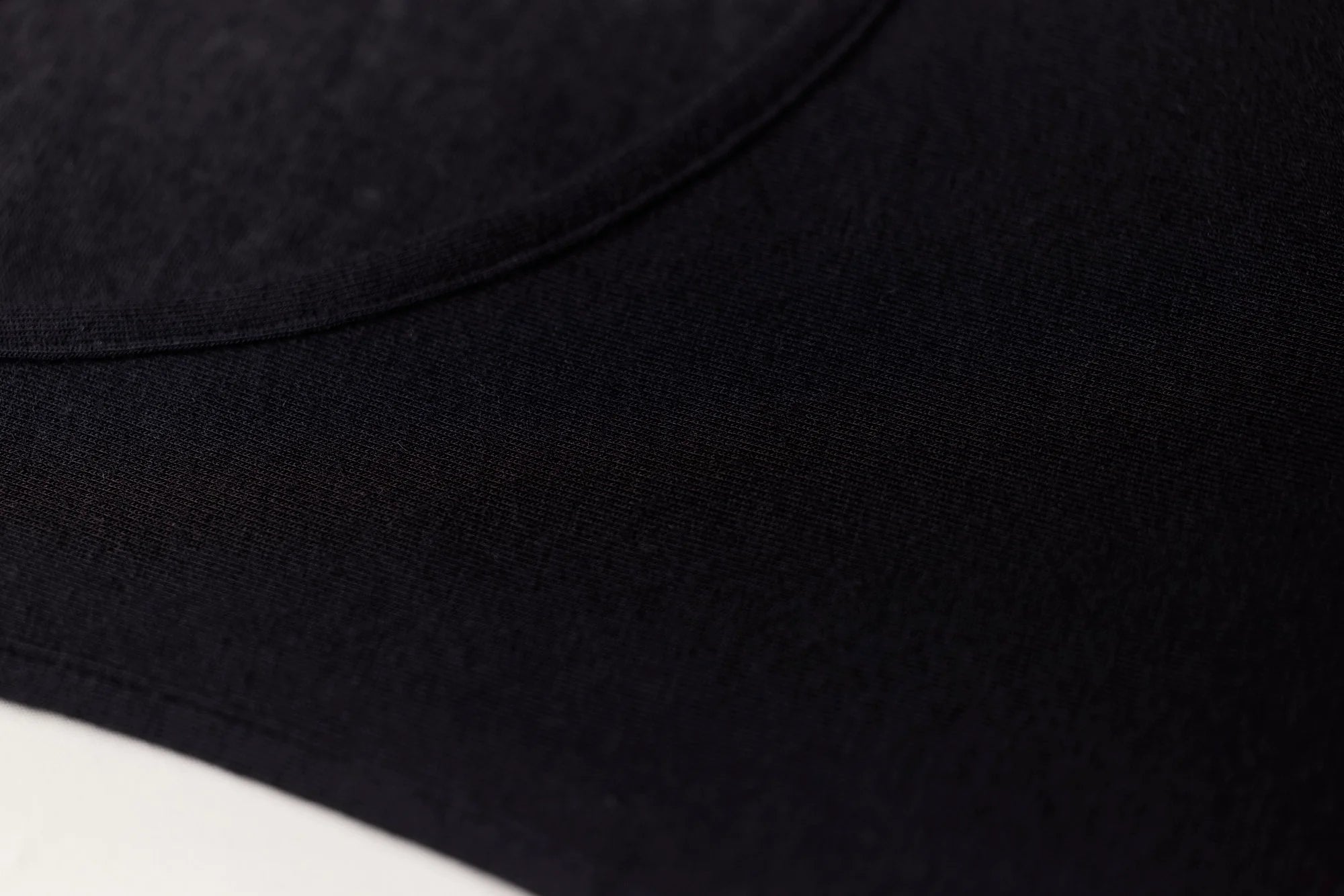 Black fabric cap with smooth slightly textured surface and visible stitching along curved brim for modal cashmere tank top